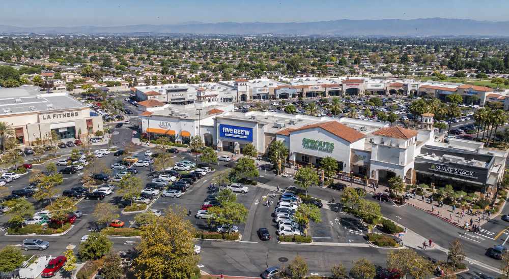 Aerial view of a busy shopping center with businesses, parking areas, roads, and commercial activity.