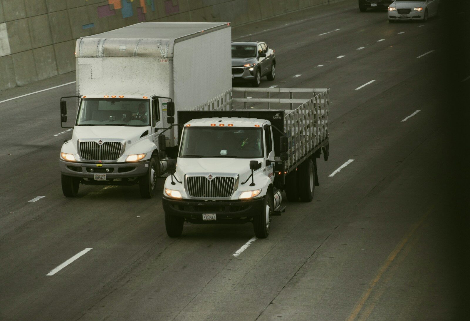 Two white trucks driving on a highway.